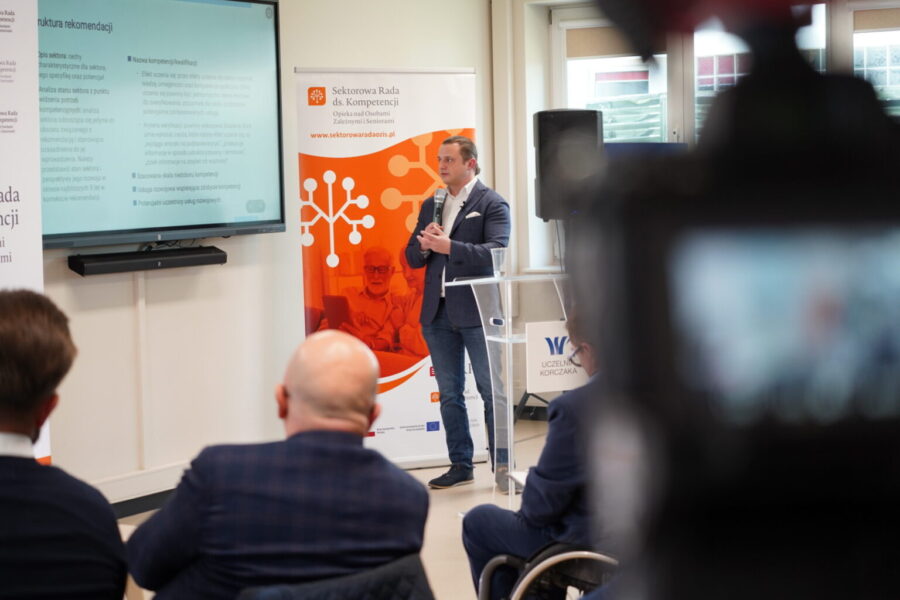 Prelegent z mikrofonem prowadzący prezentację przed uczestnikami spotkania w sali konferencyjnej