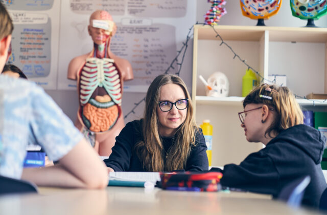 Osoby rozmawiające przy stole w sali z modelem anatomicznym w tle