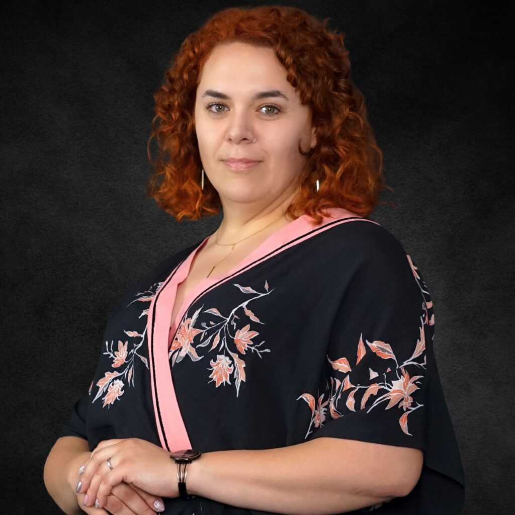 Portret kobiety z rudymi włosami w czarnej bluzce z kwiatowym wzorem na ciemnym tle
