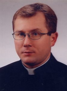 Portret księdza Mirosława Wierzbickiego w okularach i sutannie, patrzącego prosto w obiektyw.