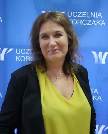 Portret kobiety na tle ścianki z logo Uczelni Korczaka