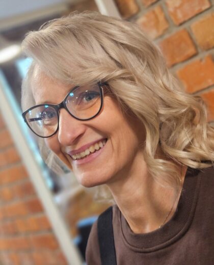 Portret uśmiechniętej kobiety w okularach na tle ceglanej ściany