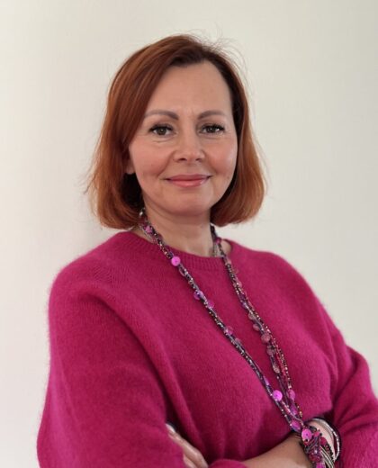 Portret kobiety w różowej bluzce i ozdobnym naszyjniku na jasnym tle