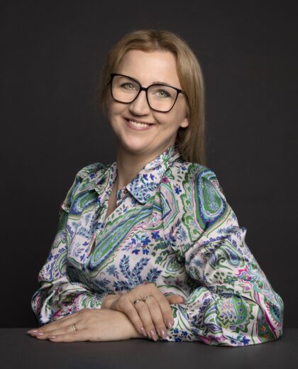 Portret uśmiechniętej kobiety w okularach i wzorzystej koszuli na ciemnym tle