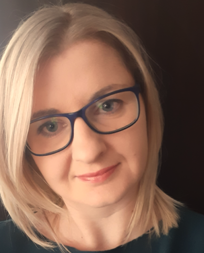 Portret uśmiechniętej kobiety z blond włosami i okularami. Dr Anna Mazur patrzy prosto w obiektyw.