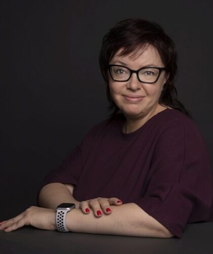Portret kobiety w okularach i bordowej bluzce na ciemnym tle