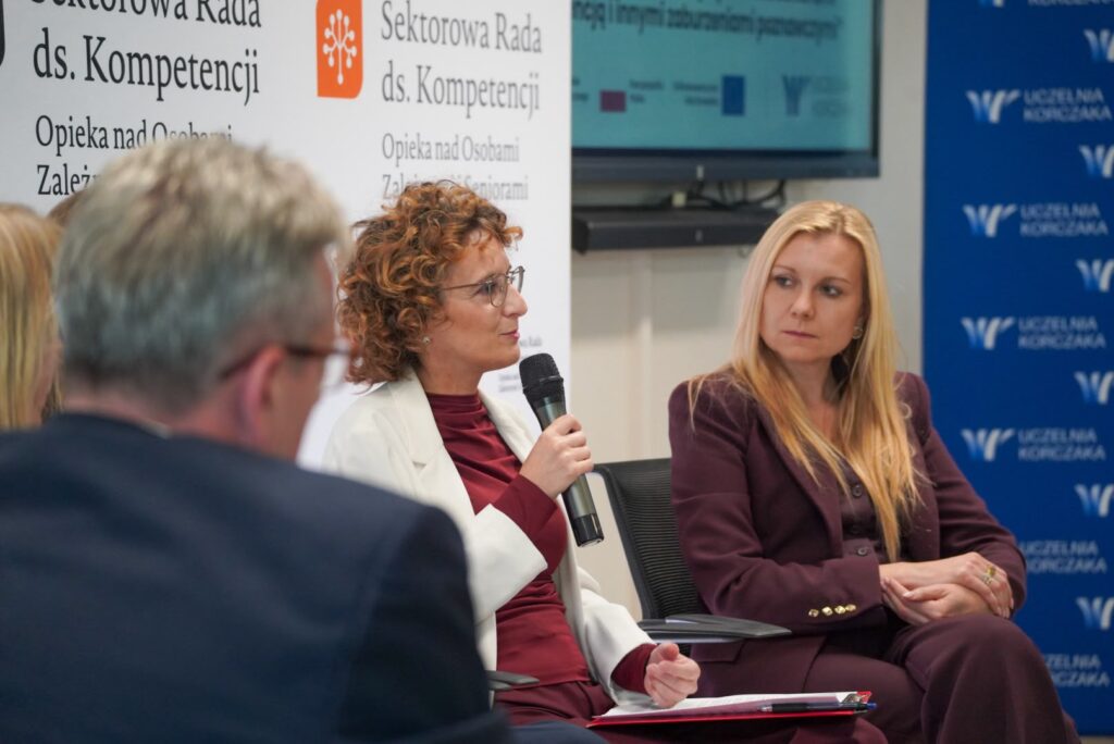 Ekspertka dr Justyna Hołyst w białej marynarce i bordowej bluzce zabiera głos podczas panelu