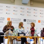 Prowadzący dyskusję i panelistki podczas rozmowy o wsparciu osób z demencją i ich opiekunów. Ujęcie ogólne na tle ścianki z logotypami Sektorowej Rady i ekranów multimedialnych.